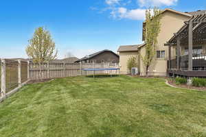 View of yard with a trampoline, a fenced backyard, central AC unit, and a pergola