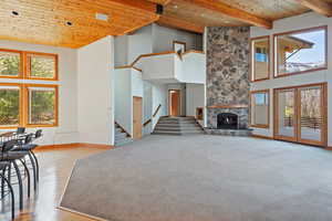 Unfurnished living room featuring stairway, a high ceiling, a stone fireplace, wooden ceiling, and baseboards