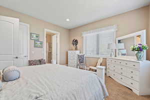 Large carpeted bedroom featuring ensuite bath and recessed lighting