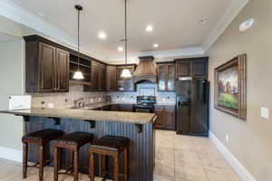 Clubhouse kitchen with range with electric stovetop, a sink, dark brown cabinetry, custom exhaust hood, and black fridge. Can be reserved for special occasions.