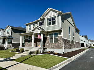 Craftsman-style home with board and batten siding, a residential view, stone siding, a front yard, and stucco siding