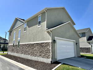 View of property exterior featuring driveway, board and batten siding, stucco siding, and stone siding