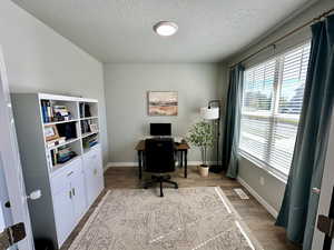 Office area with a textured ceiling, visible vents, wood finished floors, and baseboards