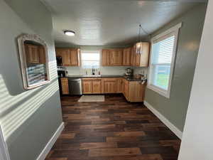 Kitchen with ample cabinets, black microwave, dishwasher, dark wood-style floors, and a sink