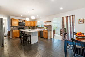 Kitchen with open shelves, appliances with stainless steel finishes, light countertops, a kitchen island, and backsplash