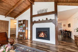 Living area featuring beamed ceiling, wooden ceiling, dark wood finished floors, a fireplace, and high vaulted ceiling