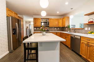 Kitchen with tasteful backsplash, open shelves, appliances with stainless steel finishes, and a sink