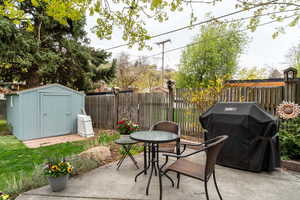 View of patio with an outbuilding, a fenced backyard, outdoor dining space, a storage unit, and grilling area