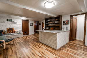Bar featuring baseboards, beam ceiling, indoor wet bar, a fireplace, and wood finished floors