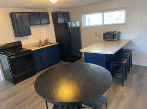 Kitchen with blue cabinetry, light wood-style flooring, black appliances, a sink, and a peninsula