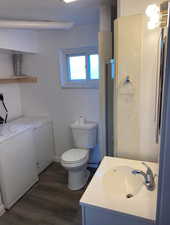 Bathroom with toilet, washer and clothes dryer, a shower with shower door, wood finished floors, and vanity
