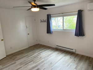 Spare room featuring light wood-style floors, baseboard heating, baseboards, an AC wall unit, and a ceiling fan