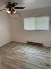 Empty room featuring a baseboard heating unit, a ceiling fan, baseboards, an AC wall unit, and wood finished floors