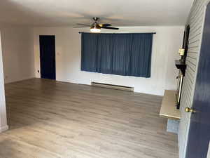 Interior space with baseboards, wood finished floors, a ceiling fan, and a baseboard radiator