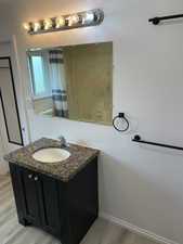 Full bath featuring wood finished floors, vanity, a shower with shower curtain, and baseboards