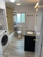 Full bath featuring wood finished floors, washer / dryer, toilet, vanity, and a textured ceiling