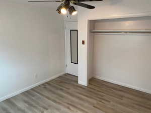 Unfurnished bedroom with wood finished floors, a closet, a ceiling fan, and baseboards