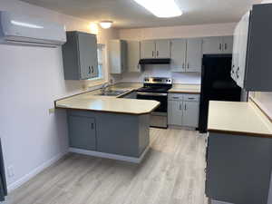 Kitchen featuring gray cabinets, under cabinet range hood, a sink, a wall unit AC, and stainless steel range with electric stovetop