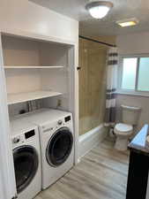 Laundry room featuring light wood-style flooring, a textured ceiling, independent washer and dryer, and laundry area