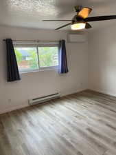 Unfurnished room featuring wood finished floors, a baseboard heating unit, ceiling fan, and a wall mounted AC