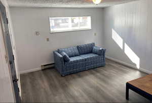 Sitting room featuring a textured ceiling, wood finished floors, a baseboard heating unit, and baseboards