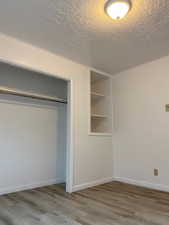 Interior space with a textured ceiling, wood finished floors, baseboards, and a closet