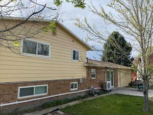 View of side of home featuring a lawn, brick siding, a patio area, and ac unit