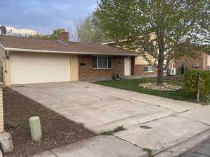 View of front of property featuring a chimney, brick siding, a garage, driveway, and a front lawn