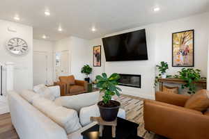 Living area featuring wood finished floors, a glass covered fireplace, baseboards, visible vents, and recessed lighting