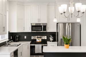 Kitchen with light countertops, white cabinetry, stainless steel appliances, and a sink