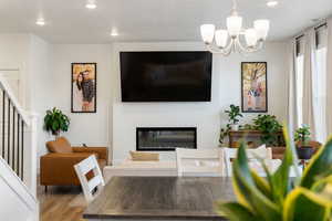 Living room with stairway, wood finished floors, a glass covered fireplace, an inviting chandelier, and recessed lighting