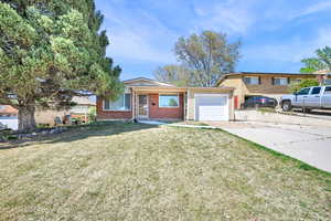 Split level home featuring a garage, brick siding, fence, a front lawn, and concrete driveway
