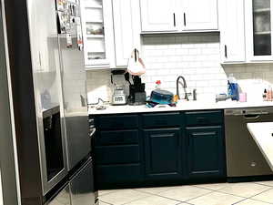 Kitchen with light countertops, stainless steel fridge, tasteful backsplash, white cabinetry, and dishwasher