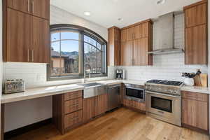 Kitchen with wall chimney exhaust hood, a sink, appliances with stainless steel finishes, and light countertops