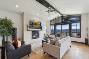 Living room featuring light wood-type flooring, lofted ceiling with beams, recessed lighting, and a glass covered fireplace