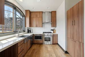 Kitchen featuring tasteful backsplash, appliances with stainless steel finishes, light wood-style floors, light countertops, and wall chimney exhaust hood