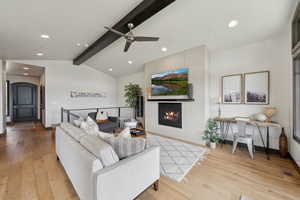 Living area featuring a fireplace, light wood-style floors, ceiling fan, and vaulted ceiling with beams