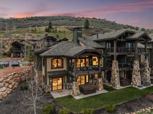 Back of property at dusk with a chimney, stucco siding, a hot tub, a patio, and a balcony