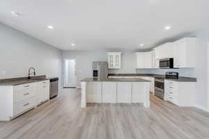 Kitchen featuring glass insert cabinets, dark stone counters, stainless steel appliances, white cabinets, and a sink