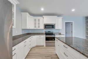 Kitchen with light wood-style floors, white cabinets, glass insert cabinets, and appliances with stainless steel finishes