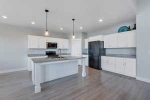 Kitchen with white cabinets, appliances with stainless steel finishes, light wood-style flooring, and a sink