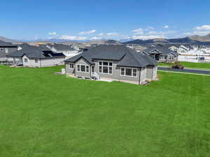 Back of house featuring a lawn, a mountain view, a residential view, and roof with shingles
