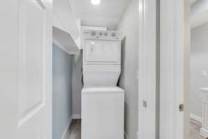 Clothes washing area with stacked washer and dryer, light wood-style floors, laundry area, and baseboards