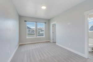 Unfurnished bedroom with light colored carpet, connected bathroom, and baseboards