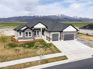 View of front facade featuring concrete driveway, stone siding, an attached garage, a porch, and a front lawn