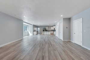 Unfurnished living room with recessed lighting, light wood-style floors, a sink, baseboards, and visible vents