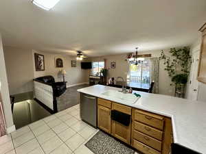 Kitchen with light countertops, brown cabinets, ceiling fan with notable chandelier, dishwasher, and a sink