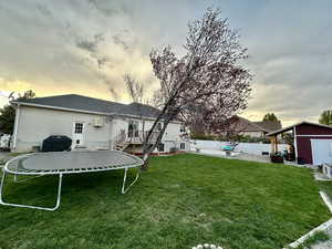 Back of house featuring a trampoline, an outdoor structure, a yard, a storage unit, and stairs
