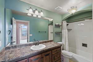 Bathroom with toilet, visible vents, shower / bathtub combination with curtain, and vanity
