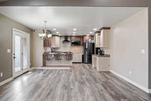 Kitchen with an inviting chandelier, wall chimney exhaust hood, light wood-style flooring, baseboards, and appliances with stainless steel finishes